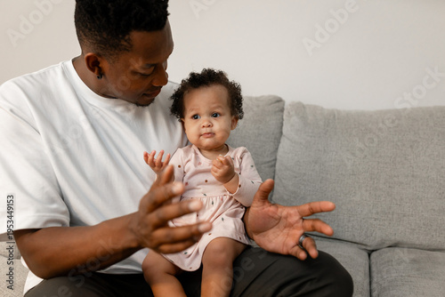 father and baby daughter on a couch playing with a smile
