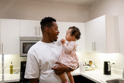 Father holding baby daughter smiling and bonding at home, multiracial family
