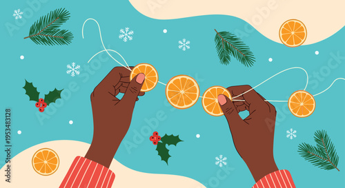 High angle view of dark skinned hands threading dried orange slices onto a string to create a natural christmas garland on a blue background.