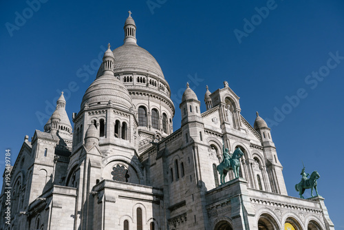 Sacré-Cœur Basilica in Montmartre, Paris, France, showing the white domes and Romano-Byzantine architecture under a clear blue sky with the equestrian statues at the entrance.
