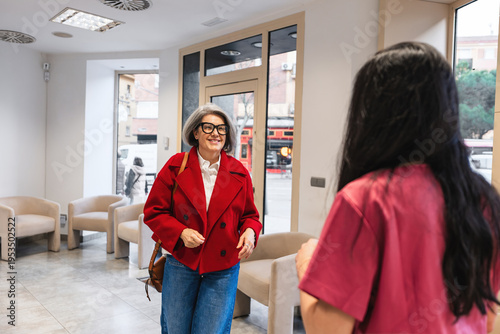 Cuadro en lienzo Woman in red jacket arriving at a modern dental clinic, being greeted by a receptionist wearing scrubs