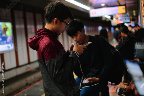 Two Young Men Using Smartphone and Power Bank in Busy Subway Station