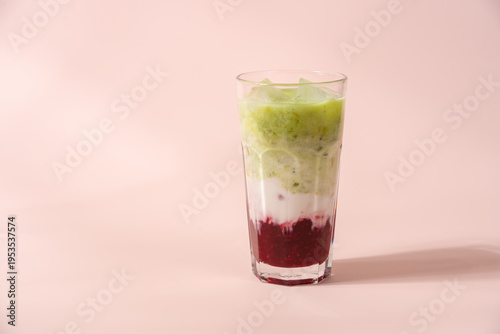 Strawberry matcha latte in clear glass on pastel light pink background with copy space, layered iced drink, minimal aesthetic