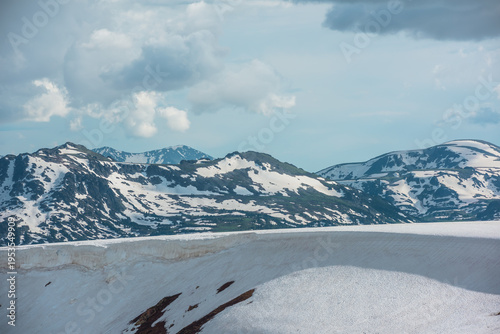 Scenic alpine landscape with sunlit snowfield with snow cornice above abyss a...
