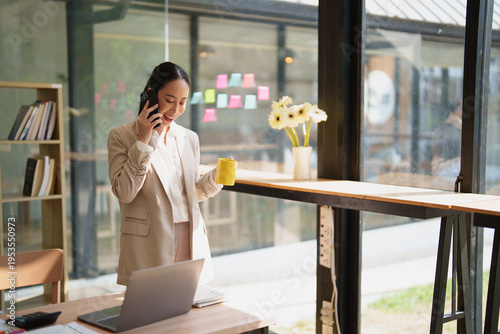 Εκτύπωση καμβά Asian businesswoman in a glass-walled modern office smiling and talking on her m