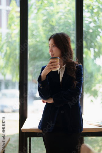 Young Asian businesswoman in formalwear stands by a large window with a disposable coffee cup, gazing thoughtfully as she plans career growth and future success in a modern office Free Download Young Asian businesswoman in formalwear stands by a large window with a disposable coffee cup, gazing thoughtfully as she plans career growth and future success in a modern office - GFXLoad