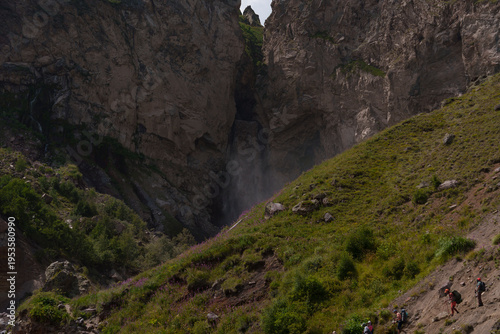 Tall waterfall between rocky cliffs in dramatic mountain landscape. Natural summer scenery with mist, green vegetation, and dramatic textures under daylight sky