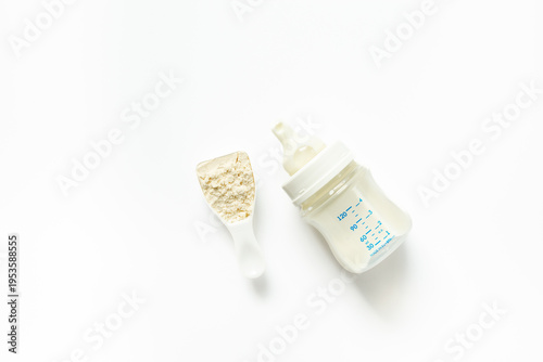 Powdered infant formula in a scoop and baby milk bottle on white background. Top view.