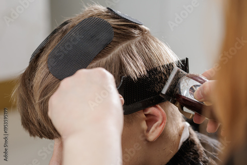 Hairdresser trimming hair with clipper over comb technique in barbershop