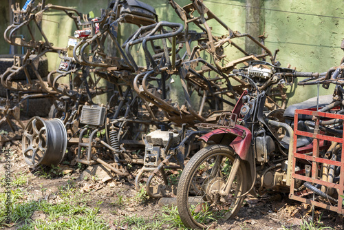 Abandoned rusty motorcycle frame pile scattered in an outdoor junkyard conveying desolate forgotten mood with broken wheel and metallic salvage parts waiting for recycling or permanent decay