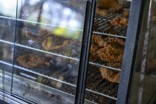 Appetizing crispy fried chicken rests on wire shelf inside warm glass display warmer, creating an inviting food presentation for hungry customers visiting restaurant for savory meat