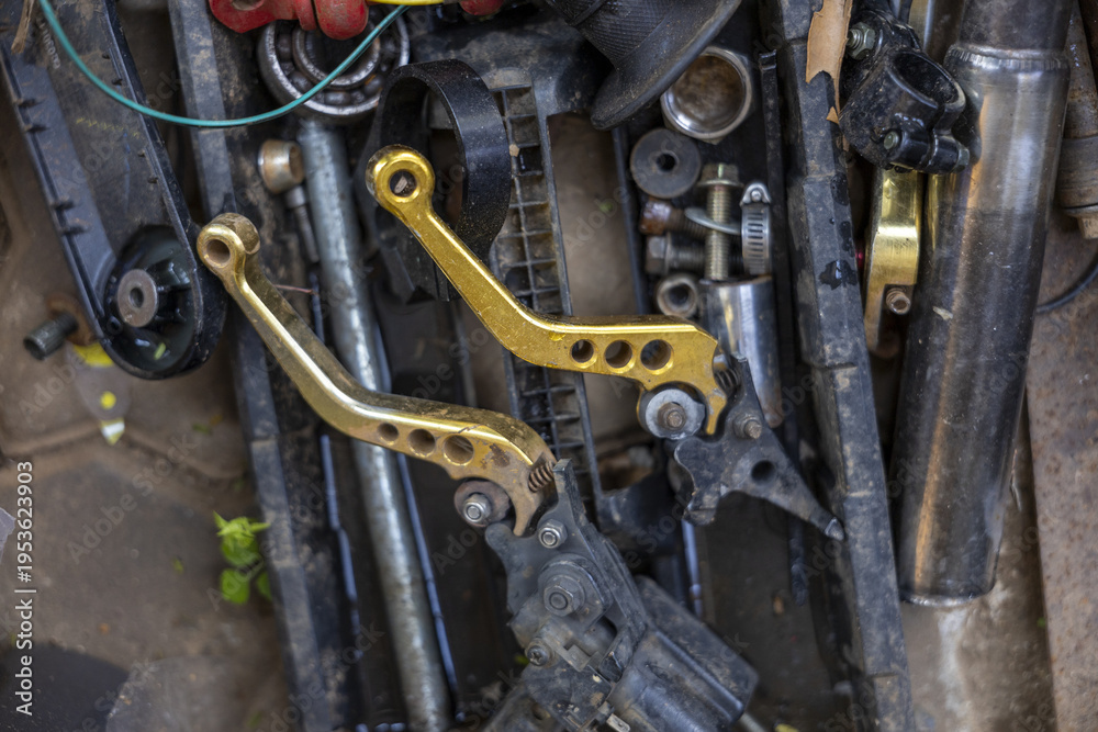 Fototapeta premium Chaotic pile featuring gold motorcycle brake lever part resting on dirty metal scrap in rough mechanic garage feeling abandoned and gritty amidst various discarded mechanical hardware component