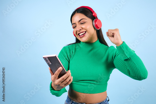 Obraz na plátně young latina woman listening to music and using headphones on blue background in