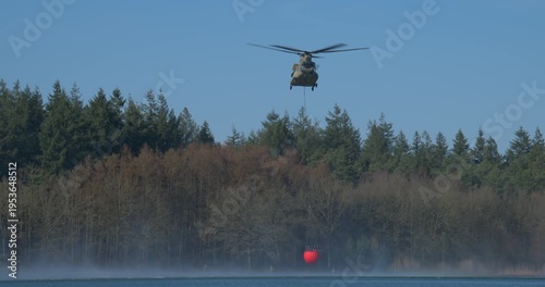 Transport helicopter of Dutch Royal Air Force carrying a water bucket for extinguishing wildfires in nature.