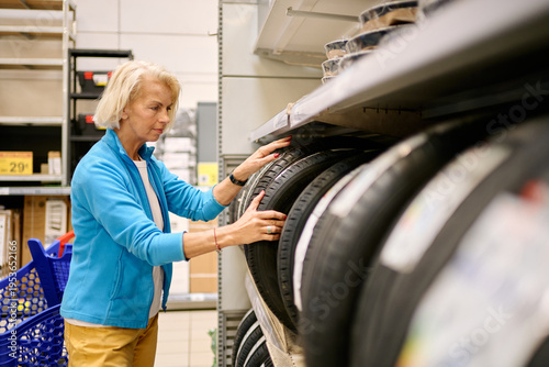 Mature woman selecting car tires in supermarket aisle