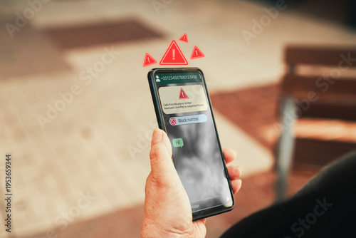 Spam text message warning on smartphone screen. Woman hand holding phone with scam alert. Phishing and cybersecurity concept.
