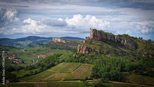 Aerial view of verdant vineyards stretching towards dramatic rocky outcrops under a brooding sky, Solutre-Pouilly, France.