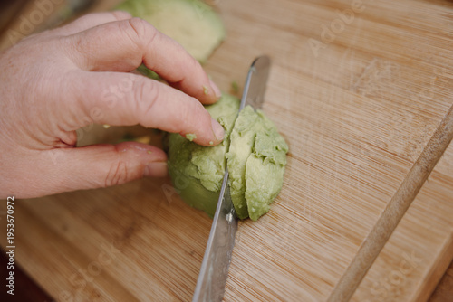 Close up of avocado being sliced with knife on wooden board