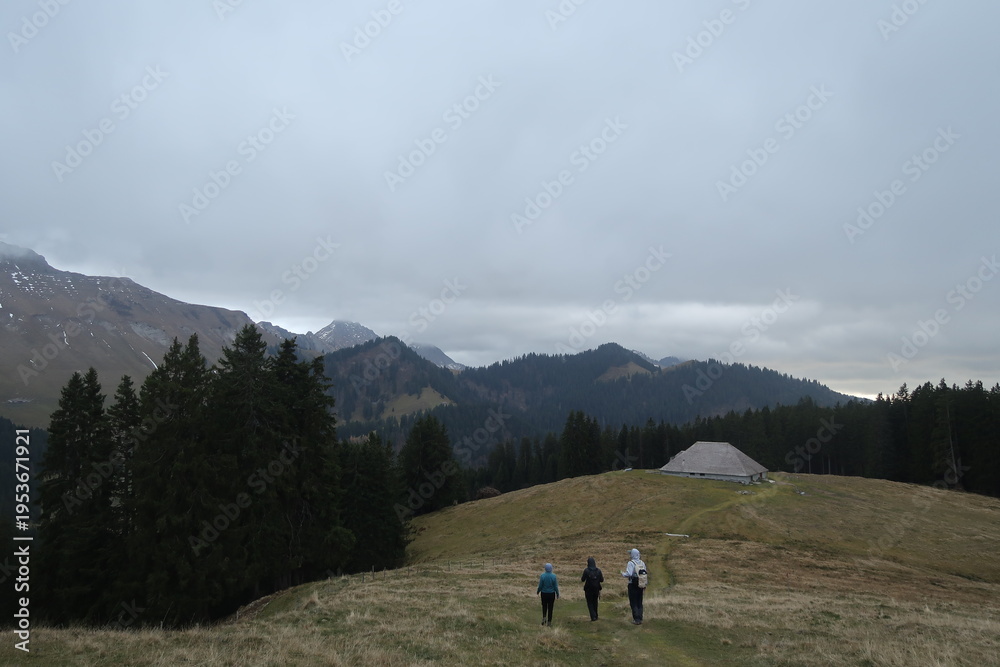 Obraz premium Hikers walking toward mountain cabin in alpine landscape under cloudy sky