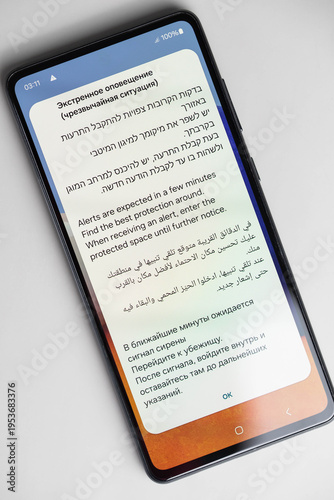 Israel emergency rocket alert notification on phone screen in Hebrew, English, Arabic and Russian, advising to go to shelter and stay in protected space. War and civil defense concept.
