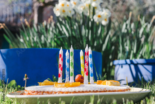 Birthday waffle cake with candles side view. Birthday cake decorated with fruits and candles on a background of green grass and white flowers