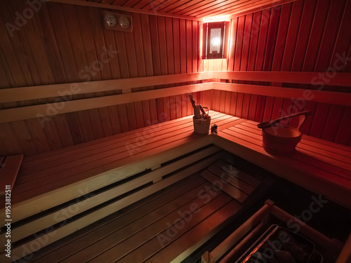Finnish brown wood sauna with moody red lights and wooden wellness equipments