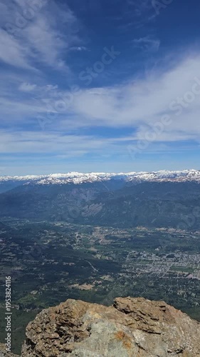 Vertical panoramic view of a vast mountain valley, town, and snow-capped peaks.