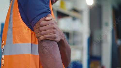 Worker in an orange safety vest experiencing upper arm pain, strain, fatigue, or injury caused by physical labor in workplace settings.