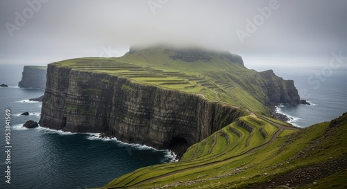 Dramatic coastal landscape with towering sea cliffs and green terraced hills under a cloudy sky.