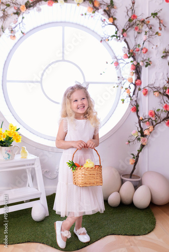Wallpaper Mural A little curly blonde hair girl in white dress with with large Easter eggs in spring interior decoration room. Happy smiling child girl with chick and carrot in basket near decorated floral window Torontodigital.ca