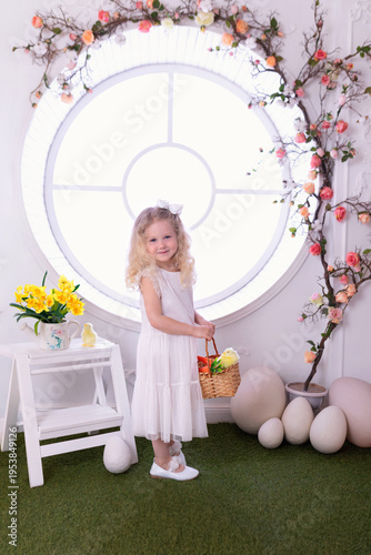 Wallpaper Mural A little curly blonde hair girl in white dress with with large Easter eggs in spring interior decoration room. Happy smiling child girl with chick and carrot in basket near decorated floral window Torontodigital.ca