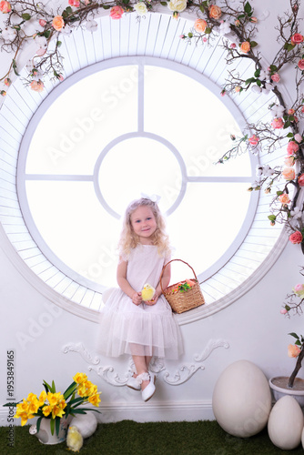 Wallpaper Mural A little curly blonde hair girl in white dress with with large Easter eggs in spring interior decoration room. Happy smiling child girl with basket holding chick in her hands near big window Torontodigital.ca