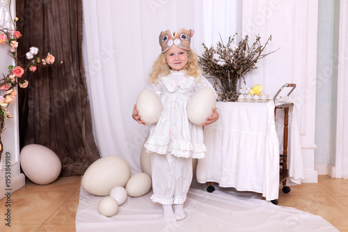 Wallpaper Mural A little blonde girl in a white dress and a rabbit ears mask on the head is smiling sit with with large Easter eggs. Happy child girl with bunny ears holding an easter egg in her hands. Vintage style Torontodigital.ca