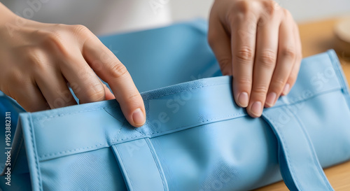 The detailed view of hands gently arranging items within a light blue tote bag