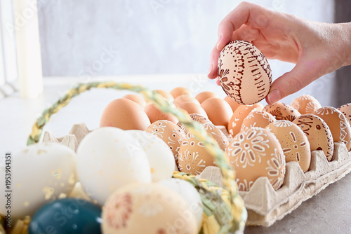 Person's hand picking a decorated easter egg from a carton full of pysanky and natural eggs