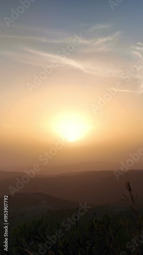 Hazy sunset over the mountain silhouettes of the Canary Islands, with the golden sun casting a warm glow through the dusty air and thin clouds creating a serene and picturesque landscape