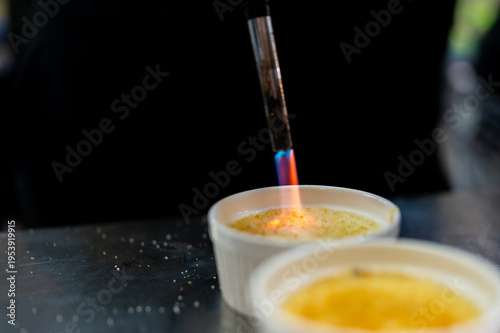 Obraz na plátně A chef uses a blowtorch to caramelize the sugar topping on a crème brûlée in a w