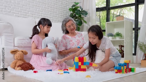Joyful Family: An intimate moment of togetherness unfolds as a grandmother and her granddaughters engage in playful building with colorful blocks in the comfort of their home.