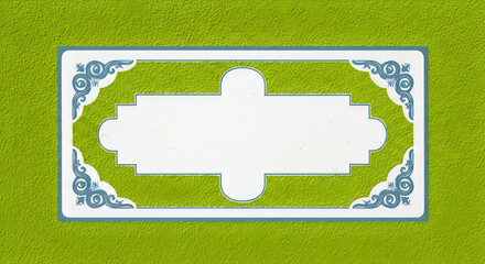 A decorative rectangular plaque with blue ornate corner patterns set against a vibrant green wall