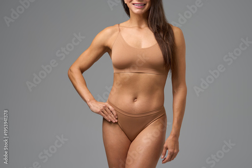 Smiling fit woman posing confidently in beige underwear on gray background