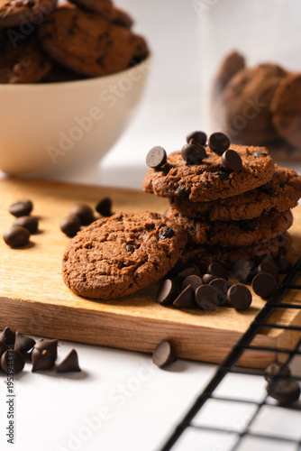 Delicious chocolate cookies with chocolate chips sprinkled on a wooden cutting board.
