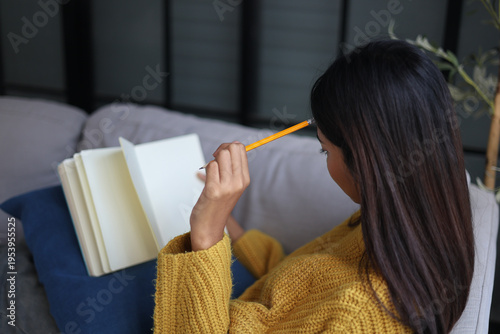 Quadro su tela Relaxed woman sitting on the sofa reading and writing in a notebook