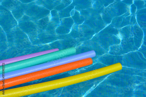 Colourful pool noodles floating on water in swimming pool