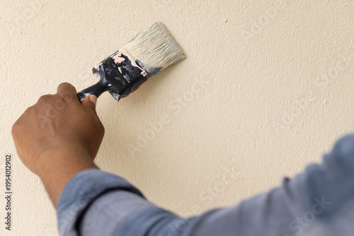 African American man painting textured beige wall at home in blue gray shirt with wide paintbrush