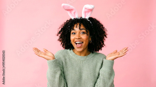 Happy young woman with delightful pink bunny ears, wearing a warm green sweater, joyfully expressing surprise or excitement with her mouth open and hands out.