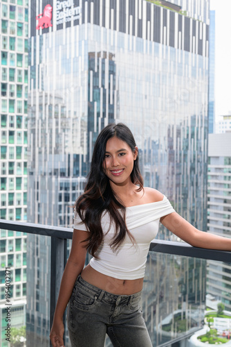 Photography Young Asian woman posing on a high-rise balcony with modern skyscrapers in Kuala
