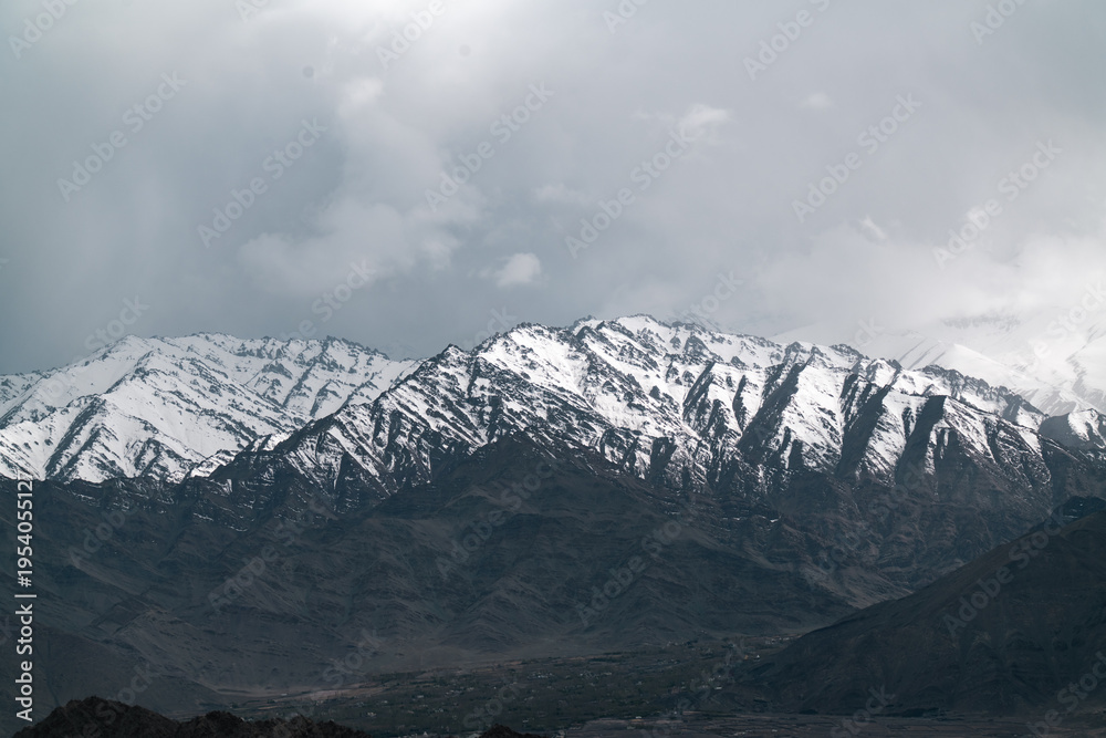 Obraz premium Snowy rugged dramatic mountain peak landscape cloudy sky winter cold remote natural outdoor scenic wilderness highland rocky serene tranquil majestic adventure