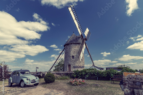 Фотография Vintage car parked near historic windmill in France