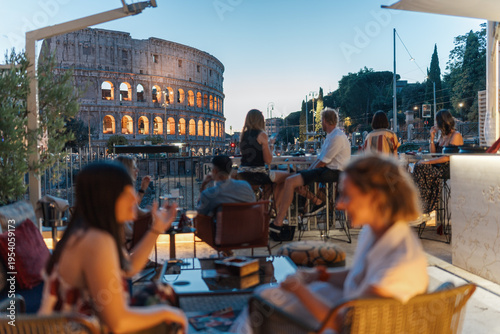 Photography Unrecognisable people enjoy drinks with a view of the Colosseum in Rome at dusk