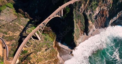 High angle view of Bixby Creek Bridge over sandy beach. Vertical drone shot of concrete bridge and waves on sandy shore at Big Sur